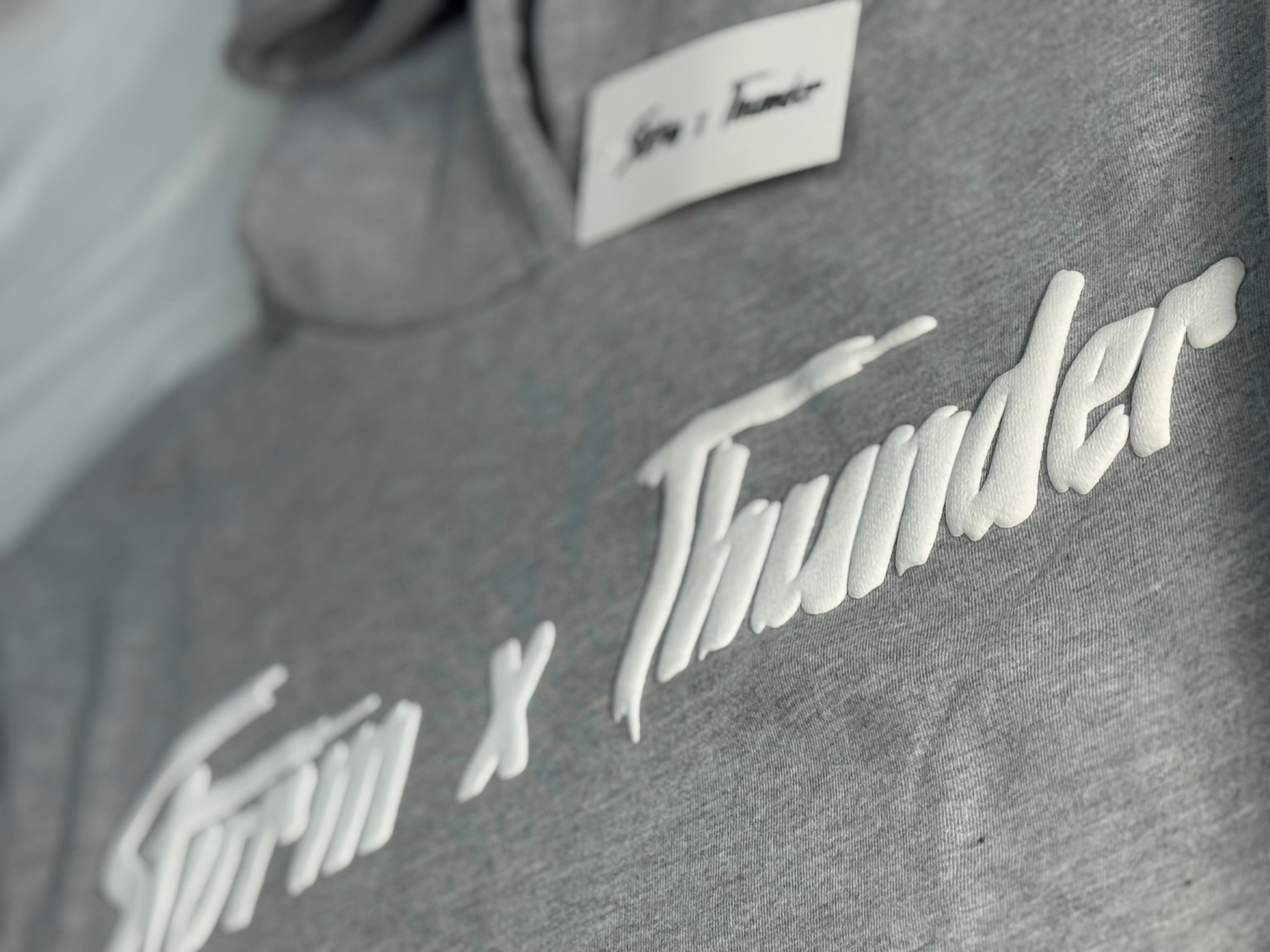 Gray hoodie with Storm x Thunder branding on a blurred background